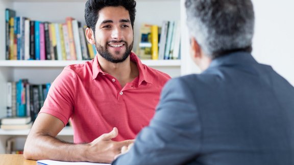Teilnehmer des beruflichen Entwicklungscoachings Gesundheit und Sozialcoaching erarbeiten Problemlösungsstrategien. Ein männlicher Brasilianer sitzt mit einem Business-Berater am Tisch.
