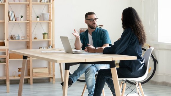 1:1 Entwicklungscoaching. Trainer sitzt mit Teilnehmerin am Tisch und erklärt etwas.