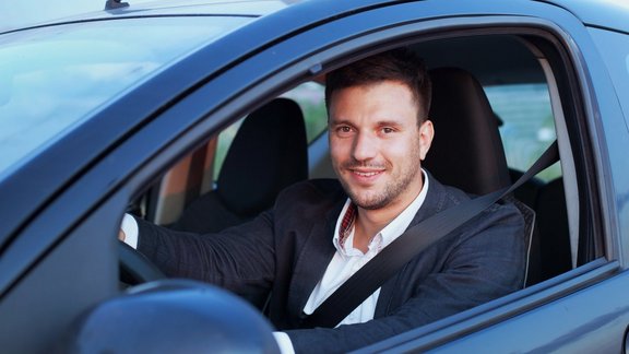 Glücklicher lächelnder Fahrer im Auto, Porträt eines jungen erfolgreichen Geschäftsmanns.
